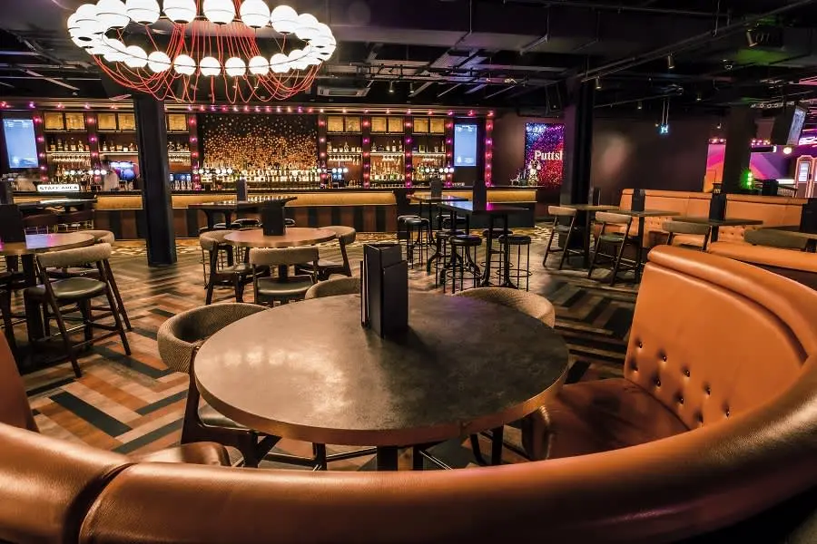 Image of a Puttshack venue's bar, dining tables, and booth